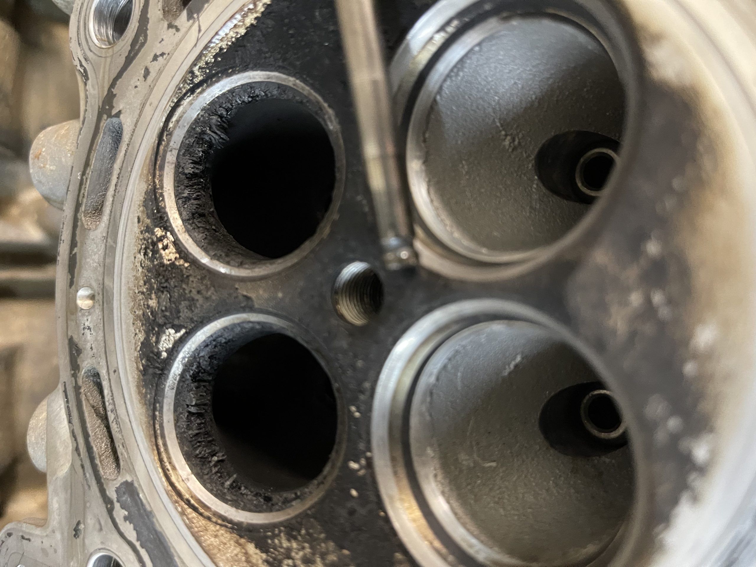 Close-up of UTV cylinder head with heavy carbon buildup around exhaust valve seats, indicating poor combustion or valve guide wear.