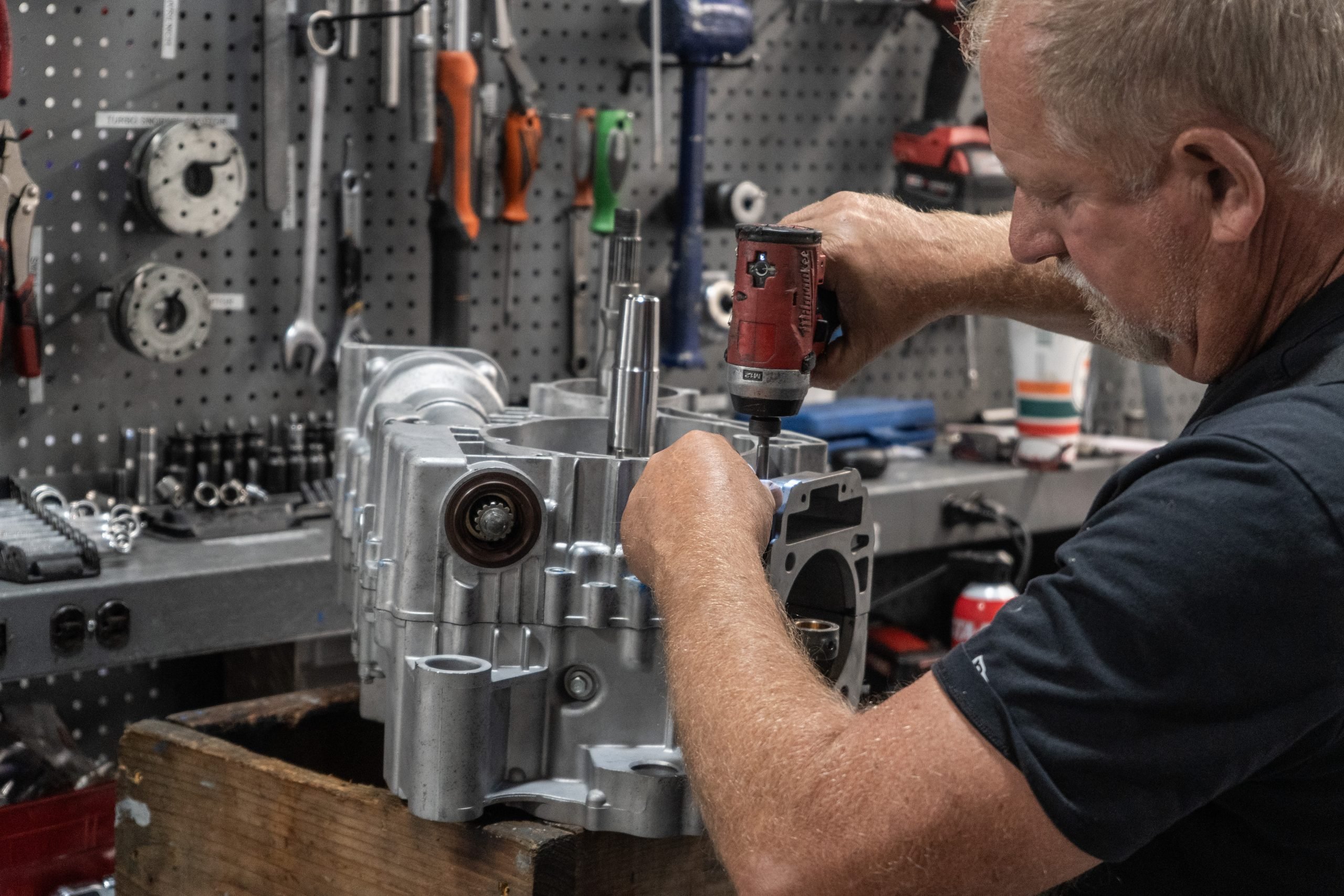 REV6 engine technician using impact driver to assemble UTV engine case during precision rebuild in shop.