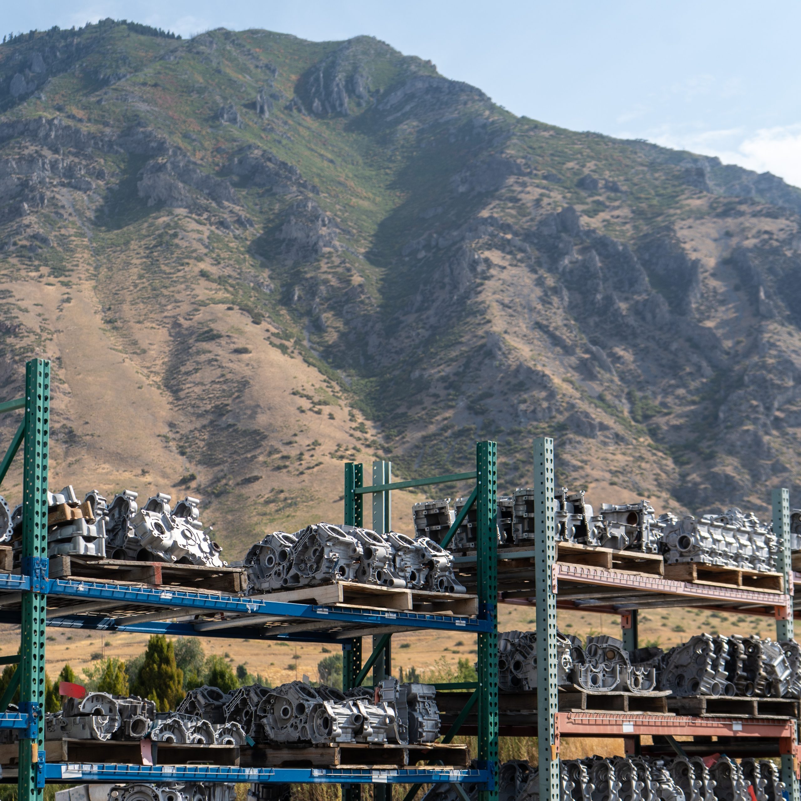 Stacks of used engine cores organized on outdoor shelves at REV6 facility, with mountain backdrop.