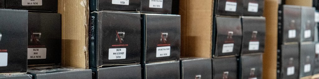 Boxes of labeled REV6 pistons for Polaris RZR and Sportsman models organized on inventory shelves.